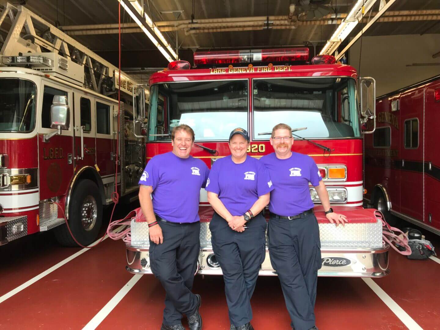 Three firefighters standing in front of firetruck.