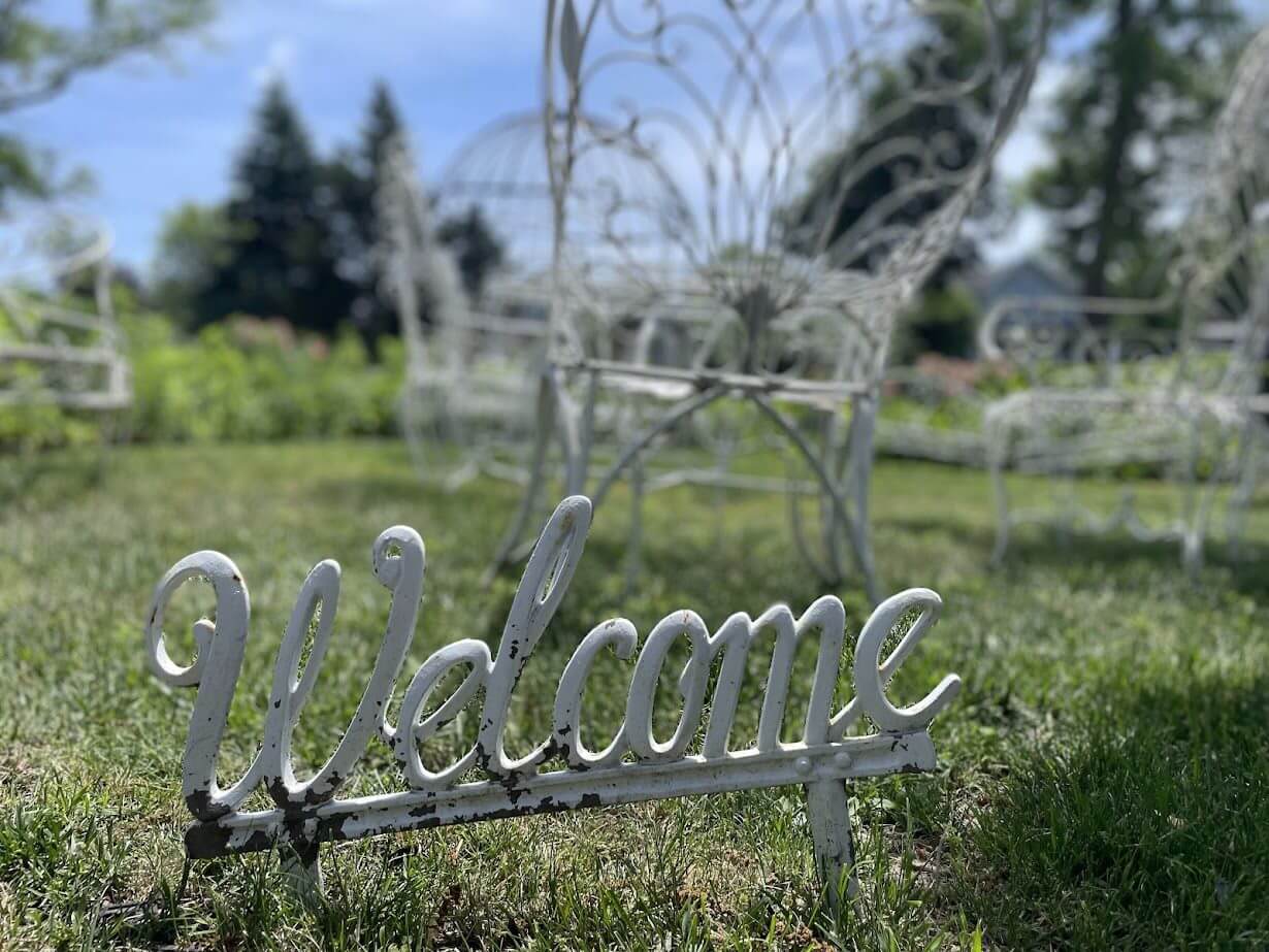 Metal "Welcome" sign with a deer figure in a garden.