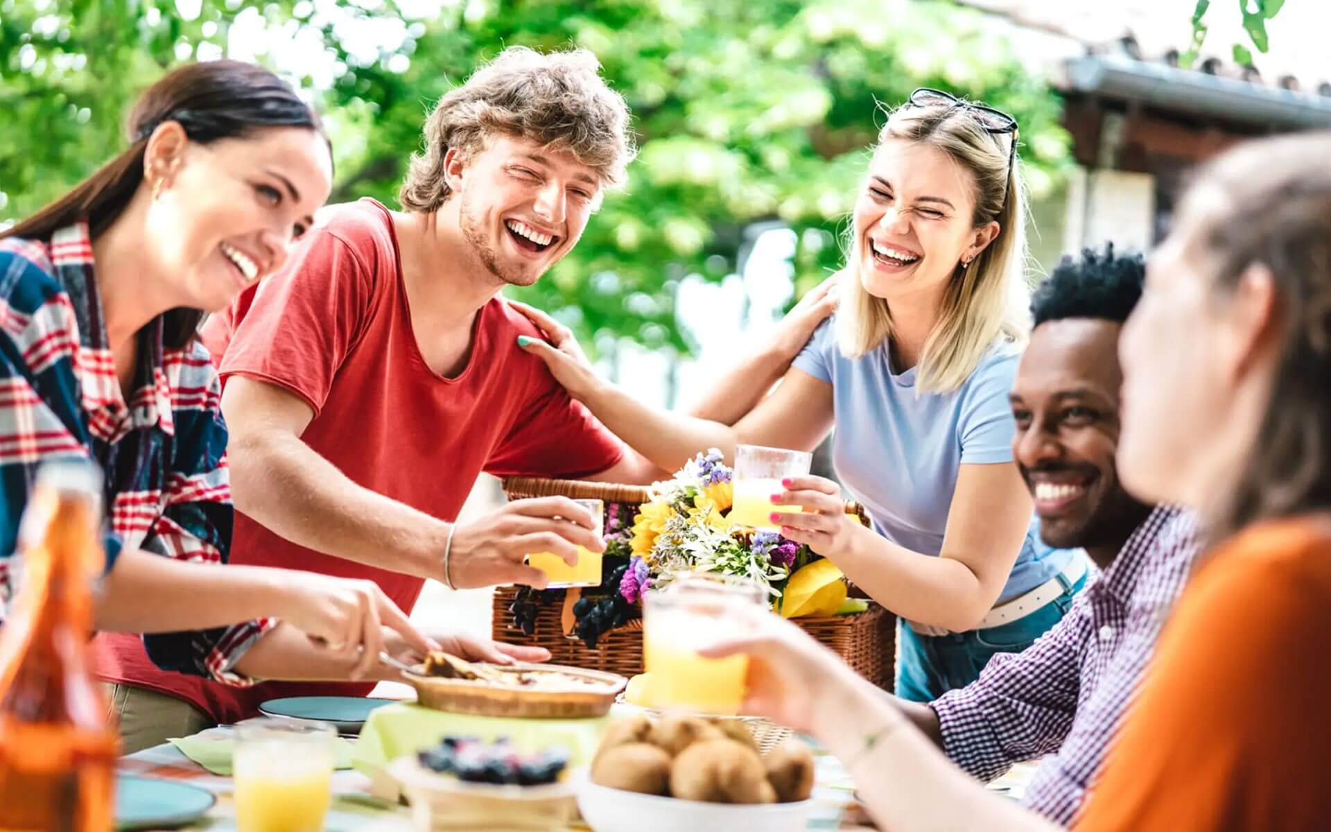 Friends enjoying drinks and laughing outdoors on a sunny day.