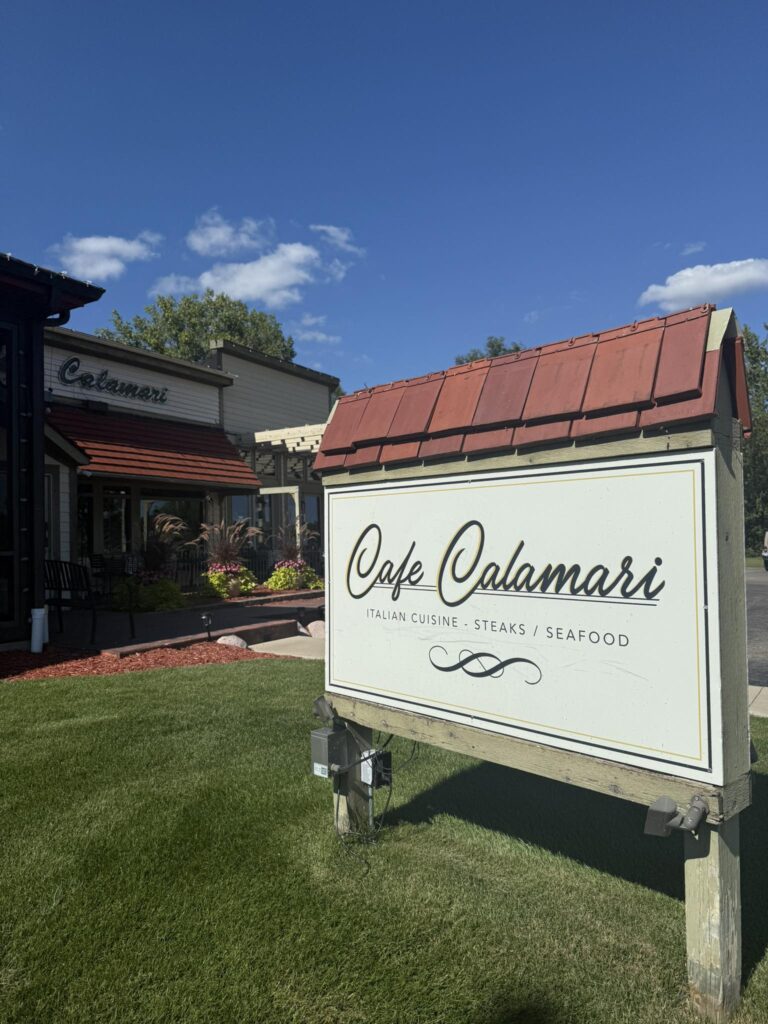 Sign for Cafe Calamari outside a sunny building with outdoor seating.