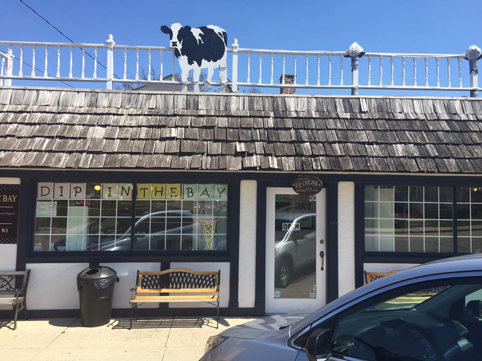 A cow statue on a rooftop above a storefront under a clear blue sky.