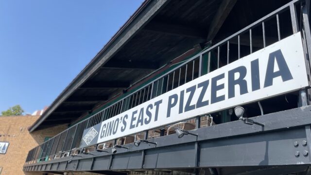 Signboard of Dino's East Pizzeria on a building.