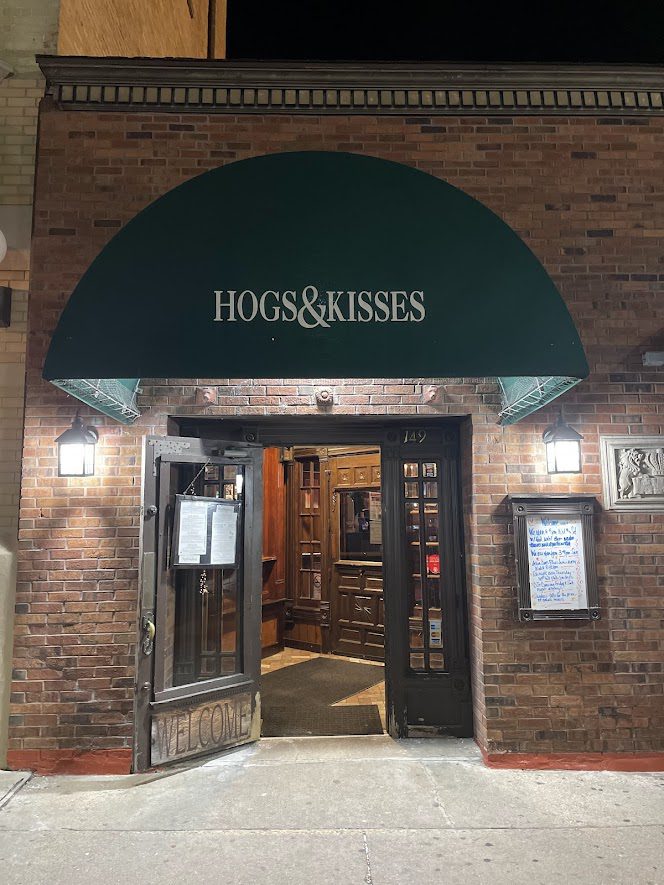 Entrance of Hogs & Kisses bar with green awning and brick wall.