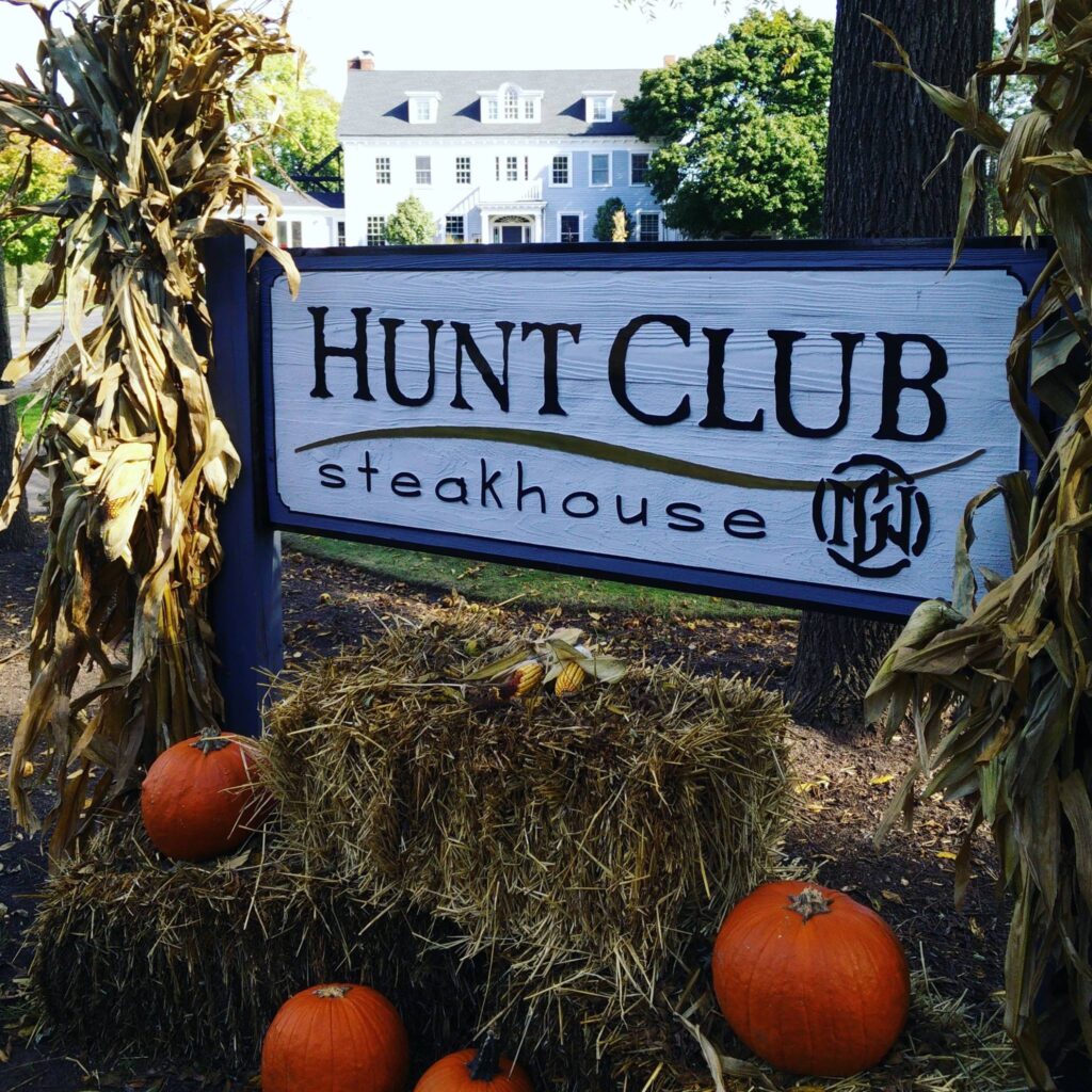 Sign for Hunt Club Steakhouse decorated with hay and pumpkins.