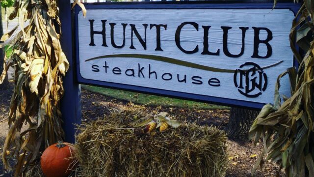 Sign for Hunt Club Steakhouse decorated with hay and pumpkins.