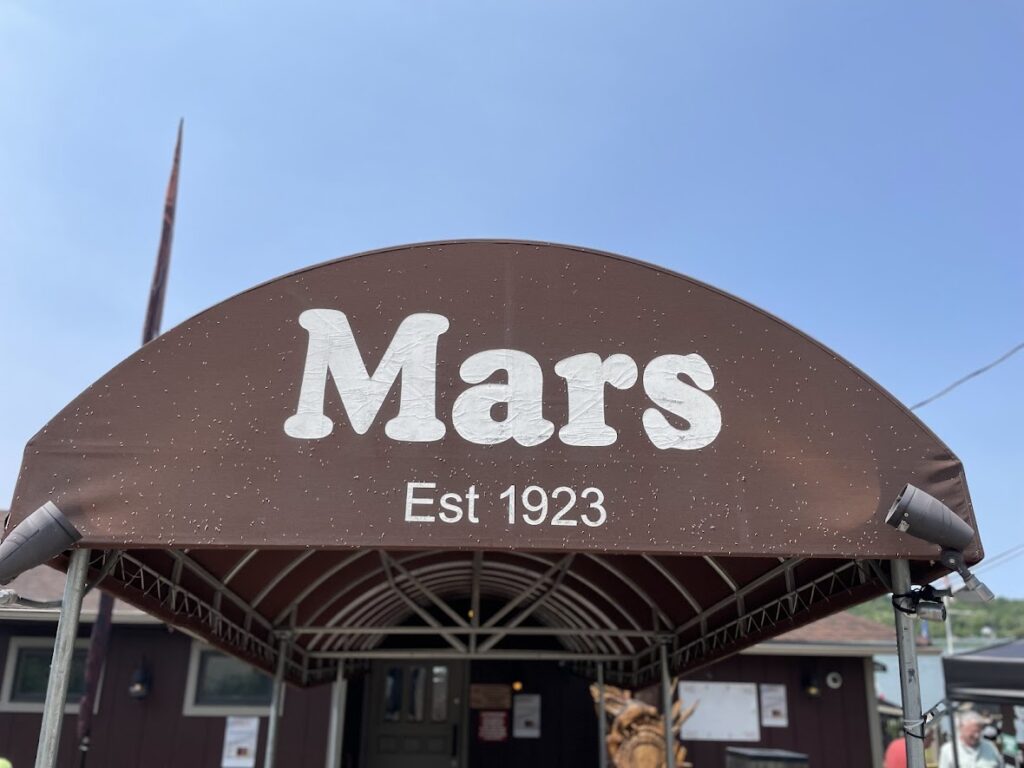 A brown awning with 'Mars Est 1923' written on it under a clear blue sky.