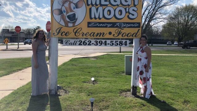 Two women posing beside a Meggy Moo's Ice Cream & Food sign outdoors.