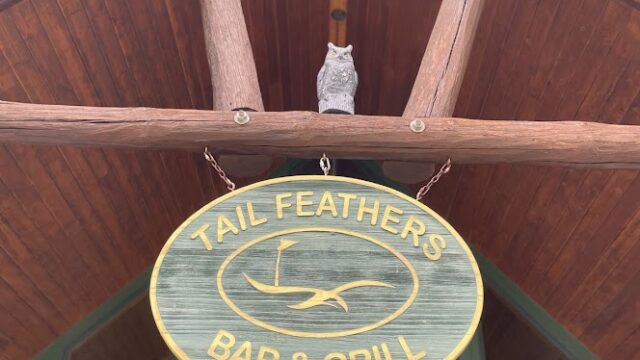 Wooden sign for Tail Feather Bar & Grill under a wooden roof.