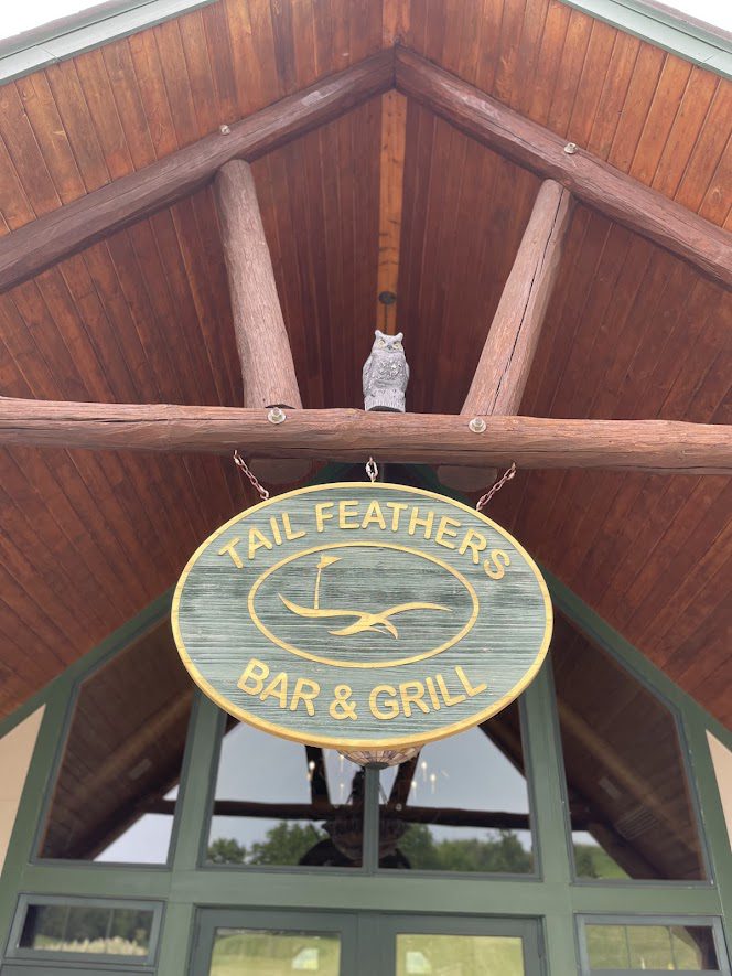Wooden sign for Tail Feather Bar & Grill under a wooden roof.