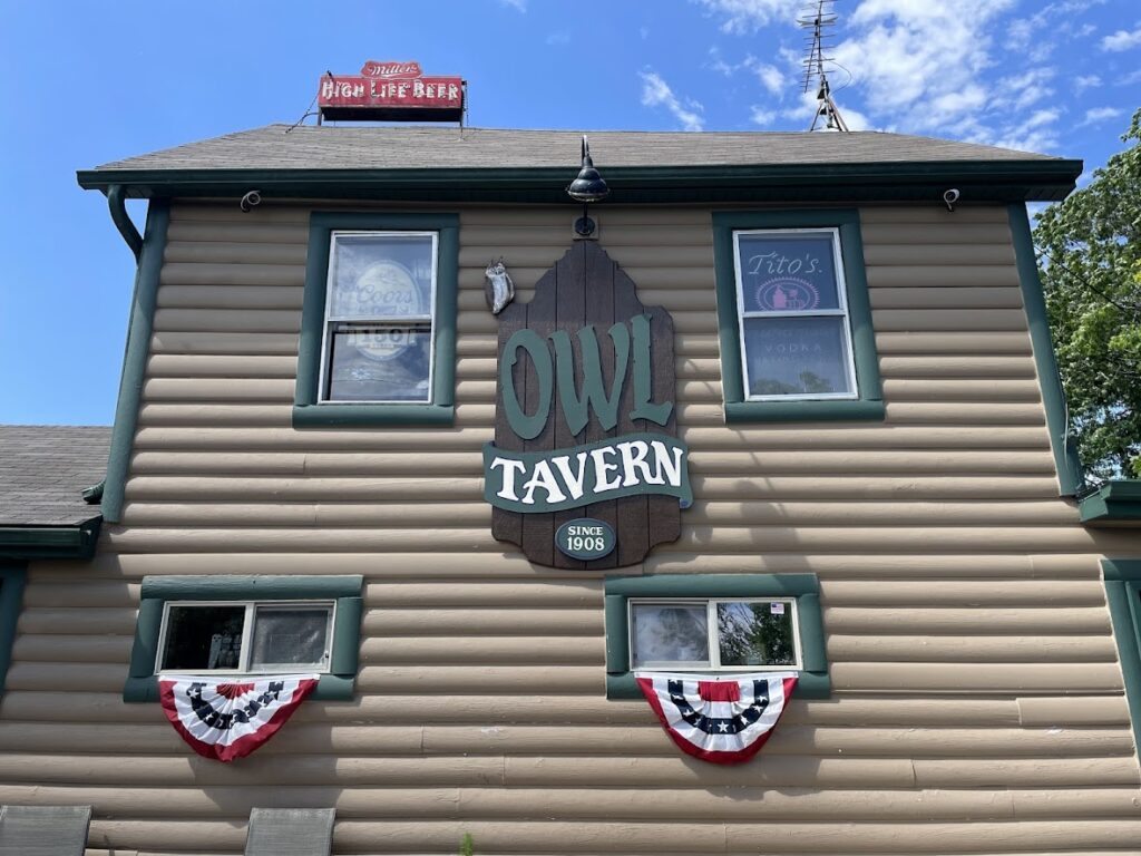The Owl Tavern sign hangs on a tan building with patriotic bunting below.