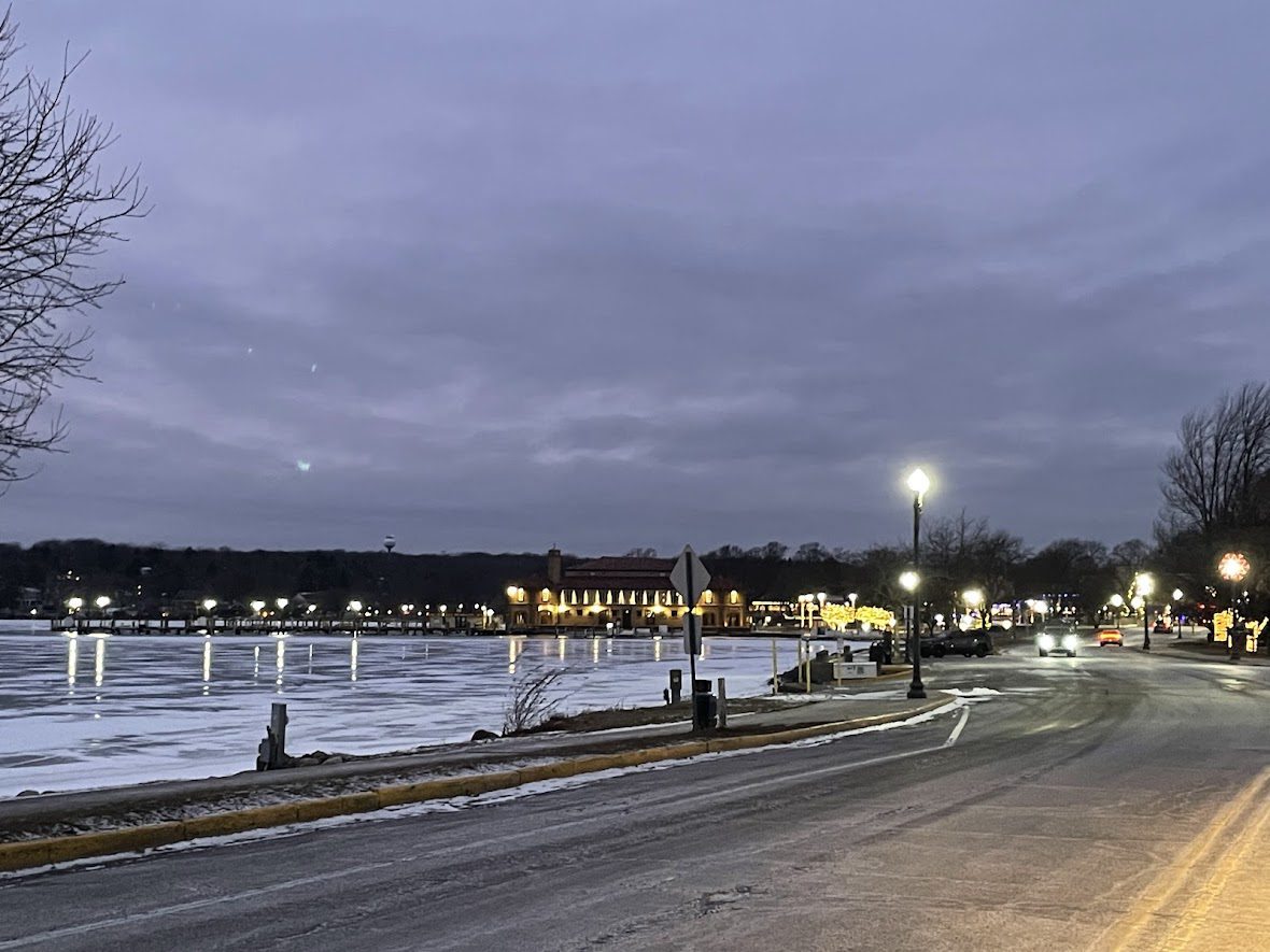 Evening view of a calm waterfront with streetlights and distant city lights.