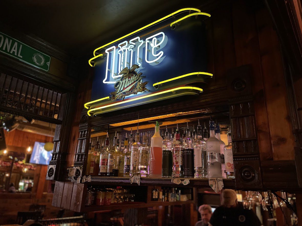 Neon Miller Lite sign glowing above a bar counter with beer taps.