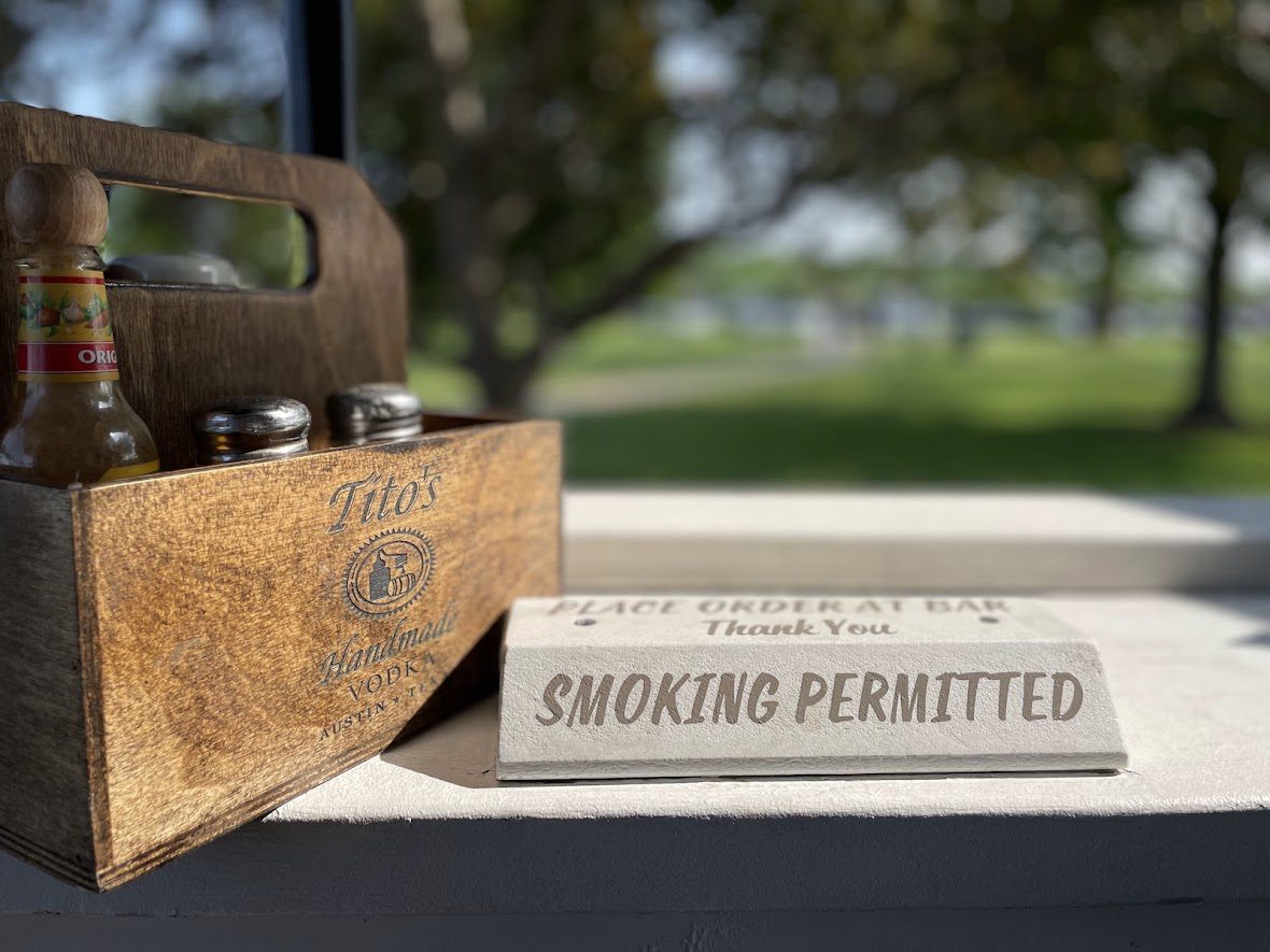 A sign on a wooden surface reads 'Smoking Permitted' in an outdoor setting.