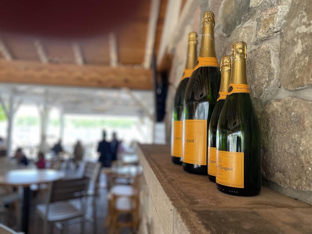 Champagne bottles lined up on a wooden shelf in a cozy, rustic venue.