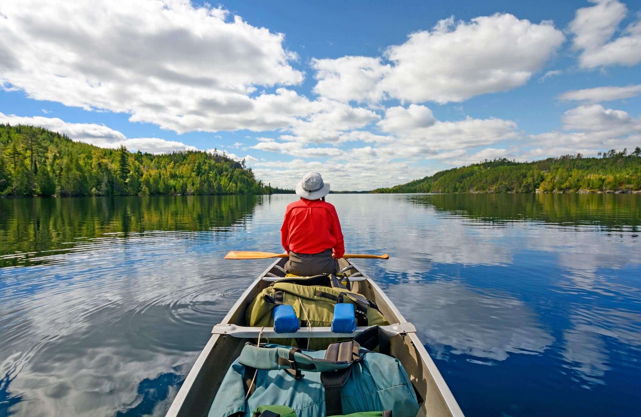 Person paddling a canoe on a calm lake surrounded by trees.