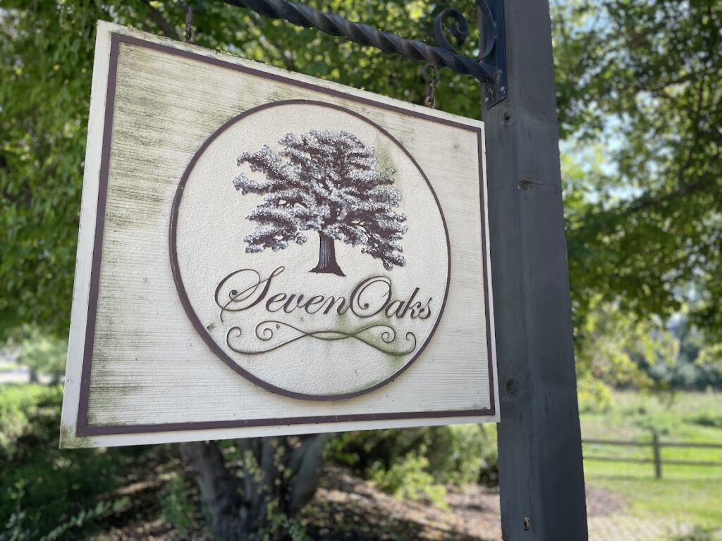 Wooden sign for Seven Oaks with a tree logo outdoors.
