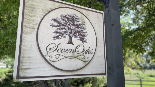 Wooden sign for Seven Oaks with a tree logo outdoors.