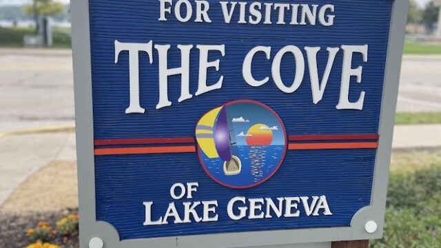 Welcome sign for The Cove of Lake Geneva with a decorative emblem.