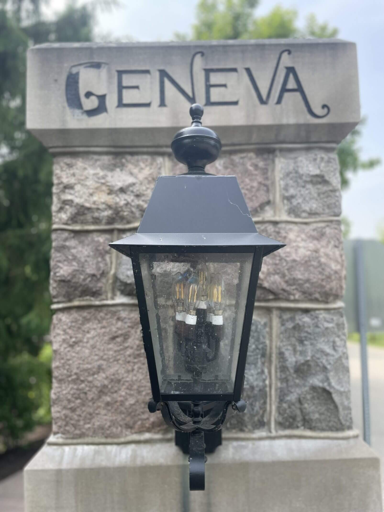 Black vintage lantern on stone pillar with 'GENEVA' plaque.